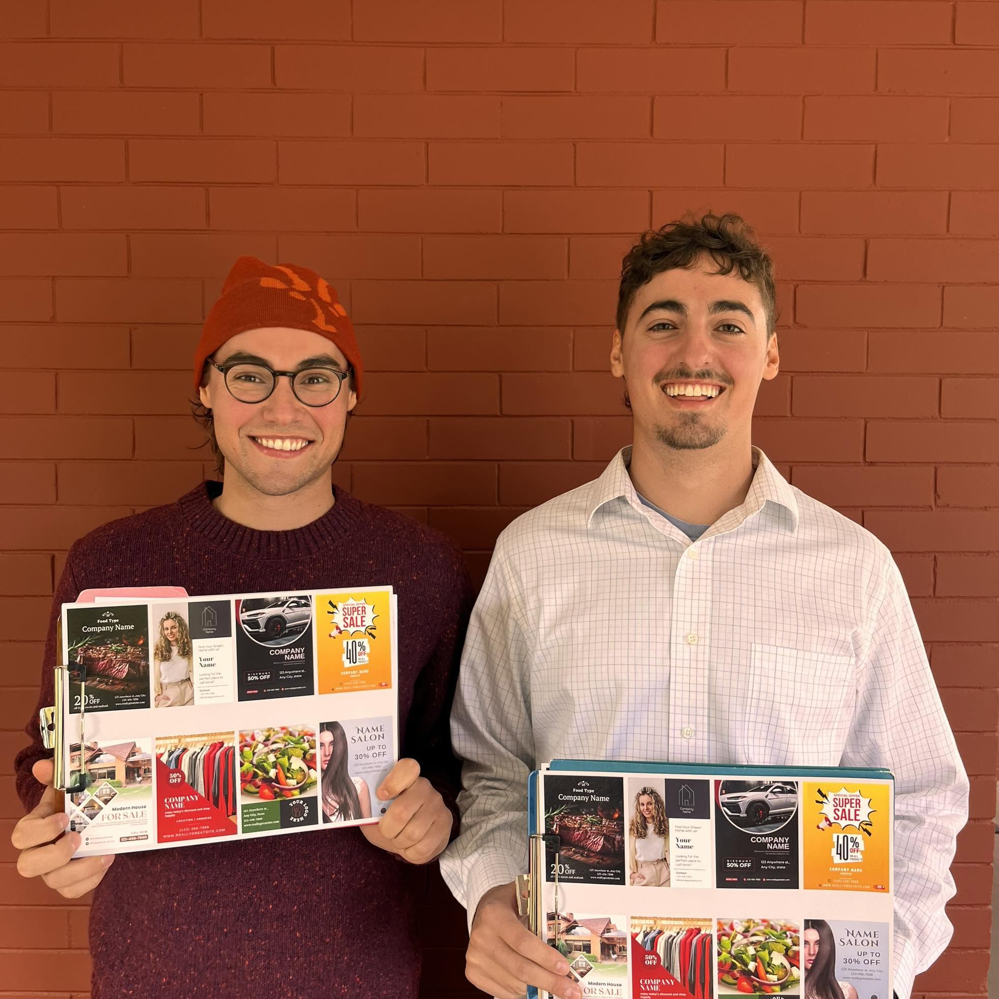 Ryan and Evan smiling and holding an example shared advertising postcard